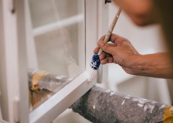 Maler bei Lackierarbeiten, es wird ein Fenster mit einem Pinsel lackiert.